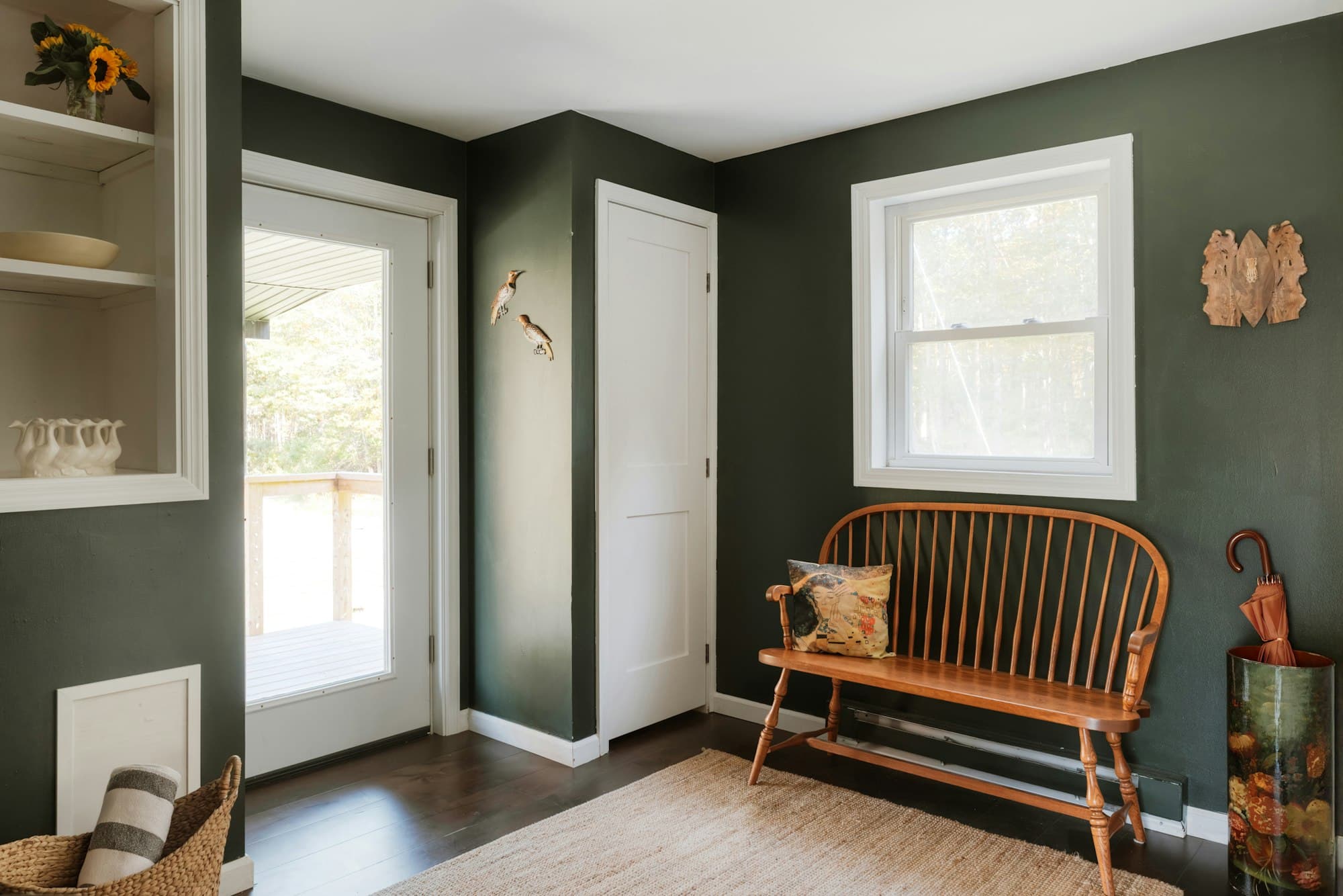 A dark, moody entryway — a wood bench against a deep green wall — the wall this piece would actually hang on.